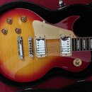 Elektrická kytara s tělem v červeno-žlutém gradientu (sunburst) umístěná v černém kufru. Nástroj má dva humbuckery s kovovými kryty, bílý pickguard a…