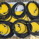 Šest svátků černých audio kabelů s konektory XLR, položených na žlutém povrchu transportního kufru. Kabelové svazky jsou stahnuté černými suchými sta…