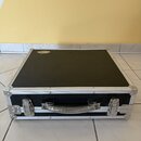 Černý transportní kufr s hliníkovými hranami a rohy. Na horní straně je nalepený oválný štítek s nápisem "DRUMCASE". Kufr má kovovou rukojeť a dva ko…
