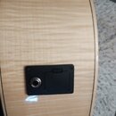 Detail zadní strany akustické kytary ze světlého dřeva s výraznou sletovanou strukturou. V dolní části je umístěn černý plastový panel s výstupem jac…