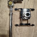 Na fotografii jsou dvě části chromovaného a černého kovového držáku na buben. Na horní části je žlutý oválný štítek s nápisem Pearl UNI-LOCK SYSTEM.…