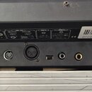 Zadní strana černého elektronického zařízení s různými konektory. Nad vstupy jsou nápisy: FIBER, DC INPUT, MIDI (INPUT a OUT), DMX OUT, AUDIO (LINE I…