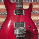 červená elektrická kytara s dvouhumbuckerovým snímačem. Na hrazdici je nápis JOE SATRIANI a na horním snímači značka Seymour Duncan. Kytara má chromo…