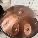 Měděný handpan s několika vyvýšenými tóny. Na povrchu je vidět logo ve tvaru kytky a nápis Harmony Handpan Sela. Nástroj vykazuje mírné povrchové zne…