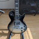 Černá elektrická kytara s gradientním přechodem do stříbrné v dolní části těla. Nástroj má dva humbuckery, čtyři ovládací knoflíky a přepínač snímačů…