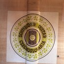 Detail štítku uvnitř akustického nástroje z jasného dřeva. Kulatý nápis v hnědé a zelené barvě obsahuje text SCHNEIDER GUITAR CZECHOSLOVAKIA. Uprostř…