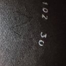 Detailní záběr na černý, texturovaný povrch materiálu. Na povrchu jsou bílým tiskem uvedena čísla 102 a pod nimi 30.