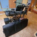 Sestava hudebního vybavení na stojanu, zahrnující klavír s nápisem roland a několik mikrofonů. K zařízení je připojeno množství kabelů a červený efek…