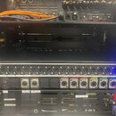 Černý rack s montovanými audio zařízeními. Větší jednotka nese vlevo logo MIDAS a vpravo nápis DL-16. Zařízení obsahuje řadu výstupů označených OUT 1…