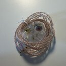 Sluchátka in-ear s průhledným plastovým pláštěm a pleteným kabelem v růžovo-stříbrné barvě. Na pravém sluchátku je viditelné kulaté logo s písmeny AV…