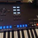 Černý digitální klavír s ovládacím panelem obsahujícím modrá tlačítka a bílé nápisy. Jsou zde sekce s názvy ASSIGNABLE, VOICE SELECT, MULTI PAD CONTR…