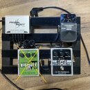 Na černém pedalboardu jsou umístěny čtyři efekty a napájecí zdroj. V horní části je bílý zdroj s nápisem POWER PLANT Junior a pětivstupním rozdělením…