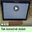 Černý kytarový kombo zesilovač s bílou síťovkou a logem Fender. Před ním na zemi leží kovový pravuhlý komponent s nečitelným nápisem. V horní části j…