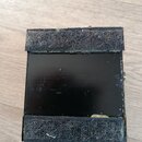 Fotografie zachycuje spodní stranu černého efekt pedálu. Na horní a dolní hraně jsou nalepené šedé suché zátěže (velcro). Povrch je černý, s několika…