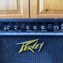 Černý kytarový zesilovač s ovládacím panelem a mřížkou. Na přední straně je žluté logo Peavey. Ovládací panel obsahuje knoflíky s nápisy VOLUME, PRE,…