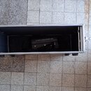 Otevřený hliníkový transportní kufr, v němž je umístěn černý zesilovač. Na horní straně zařízení je bílý nápis GALLIEN-KRUEGER. Kolem zesilovače jsou…