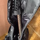 Černá elektrická kytara v černém polstrovatém pouzdře. Na hlavě nástroje je bílý nápis Harley Benton Custom Series. Hриф kytary má hnědý prstový hrac…