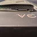 Na fotografii je černý, plochý elektronický modul s žebrovaným horním povrchem. Na boku je viditelný nápis EV3A | NU AUDIO a malý slot. Modul leží na…