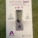Krabice s produktem APOGEE jam+. Na obalu je zobrazen šedý USB instrumentní vstup s headphone output a logem APOGEE. Text na krabici uvádí: „Professi…