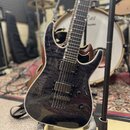 Elektrická kytara s tmavým, žilnatým povrchem těla a hnědými hranami. Nástroj má dva humbuckery s nápisem emo a tři ovládací knofíky. Kytara je umíst…