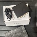 Černý kovový box s několika zlatými konektory na zadní straně, položený na bílém kartónovém obalu. Na krabici je uveden nápis s.m.s.l a text Foshan S…