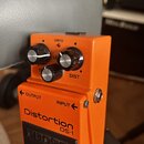 Oranžový kytarový efekt s nápisy Distortion DS-1 a logem BOSS na spodním černém pedálu. Na horní části jsou tři ovládací knoflíky s popisky LEVEL, DI…