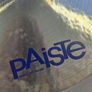Detailní záběr na kovový činel v přirozené zlatavé barvě s viditelným broušením. Na povrchu je modrý nápis PAiste a pod ním menší text MADE IN SWITZE…