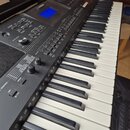 Černý digitální klavír s bílými a černými klávesami. Na horním panelu je modrý displej a nápis Yamaha. Nástroj obsahuje řadu tlačítek, posuvníků a dv…