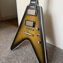 Elektrická kytara s tělem ve tvaru V v žlutém gradientním provedení s černým okrajem. Nástroj má dva humbuckery, tři otočné knofíky a jeden přepínač.…