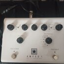 Bílý kytarový pedál s nápisem AMPED 1 a podepsaným textem DEPT. 10 | 100W AMP PEDAL. Obsahuje šest černých otočných ovátků s popisky GAIN, BASS, MIDD…