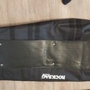 Černý polštovovaný pouzdro na hudební nástroj s rýhovaným povrchem v dolní části. Na spodním okraji je bílý nápis ROCKBAG by Warwick. Pouzdro má něko…
