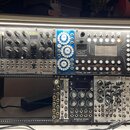 Fotografie zachycuje modularní syntetizátor v černém racku. V horní části jsou moduly s nápisy bohm, ohmforce, vpmode a Eloquencer od značky Winter M…