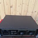 Černý výkonový zesilovač s nápisem SEAK PA 410 POWER AMPLIFIER. Na předním panelu jsou dvě otočné volitka označená jako VOLUME LEFT a VOLUME RIGHT, p…