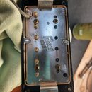 Fotografie zachycuje spodní stranu kytarového snímače s kovovou základnou a černým plastovým rámem. Na kovovém povrchu je vyražen nápis Gibson USA. J…