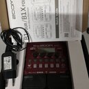V kartonové krabici se nachází červený efektový procesor s nápisem B1 FOUR ZOOM Multi-Effects Processor. Zařízení má pět číselných tlačítek, displej…
