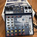 Míchací pult Soundcraft NOTEPAD-8FX v tmavě modré barvě, umístěný před svým původním bílým krabicem s nápisem Notepad 8FX. Na horní straně jsou vstup…