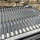 Šedý mixážní pult s mnoha posuvníky a otočnými knoflíky v různých barvách (černá, modrá, žlutá). Na spodní liště je vidět nápis Soundcraft Spirit Fol…