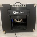 Černý kytarový kombo zesilovač s nápisem Quilter na předním panelu. Horní část obsahuje ovládací prvky v podobě bílých otočných knoflíků. Nástroj je…