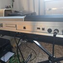 Zadní strana stříbrného digitálního klavíru s nápisem YAMAHA. Jsou zde viditelné konektory LAN, USB TO DEVICE, USB TO HOST, MIDI IN a OUT, AUX IN L+R…