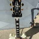 Bílá polodublová elektrická kytara značky Epiphone s gold hardwarem. Na hlavě je bílý nápis Epiphone a černá ozdobná vložka. Hриф má vložky z perlece…