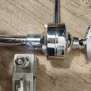 Detail chromovaného kovového spojovacího mechanismu s utahovacím knoflíkem ve tvaru křídla. Součástí je kovová tyč a v dolní části je vidět stříbrný…