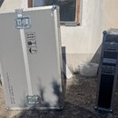 Dvě transportní bedny s kovovými hranami a vrchními zámky. Větší šedá bedna má na boku nápisy PROPERTY OF PHILIPS EUROSERVICE a DEPOSIT EURO 500,00 o…