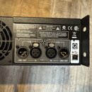 Zadní strana černého elektronického zařízení s ventilátorem. Jsou zde čtyři konektory XLR, popsané jako INPUTS (IN) a LINK / OUT pro kanály CH1 a CH2…