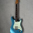Modrá elektrická kytara s tvarem typu Stratocaster a bílým pickguardem. Na hlavě hředu je viditelné logo Fender. Kytara má tmavý hmatník a tři snímač…