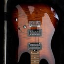 Elektrická kytara s hnědým lakem s viditelnou strukturou dřeva, umístěná v černém tvrdém kufru. Nástroj má dva humbuckery s nápisem „Duesenberg“ a ch…