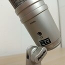 Stříbrný kondenzátorový mikrofon s kovovou mřížkou. Na těle je nápis E205U, vedle vstupu pro sluchátka se nachází štítek s označením CN382 a symbolem…