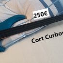 Modrá elektrická basová kytara s černým hmatníkem a kovovým mostem. Na těle nástroje jsou čtyři ovládací knofíky a jeden přepínač. V popisu na fotogr…
