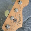 Hlava basové kytary z přírodního světlého dřeva se čtyřmi chromovanými ladičkami. Na povrchu je černý nápis Fender, pod ním text MADE IN U.S.A. a ved…