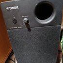 Černý reproduktor s látkovou maskou v dolní části. Na horním panelu je bílé logo YAMAHA, tlačítko napájení a otočný regulátor s nápisem BASS VOLUME a…