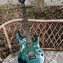 Kytara s tmavě zeleným kovovými lakem a hnědým hmatníkem. Na hlavě je bílý nápis "Schecter". Nástroj má dva humbuckery a fixační most. Povrch laku je…